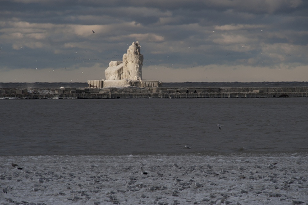 A small break in the clouds overhead allows sunlight to momentarily illuminate the ice-covered Cleveland Harbor West Pierhead Lighthouse, Dec. 14. All across the Great Lakes, high winds and subzero air temperatures caused waves to crash onto lighthouses and other aids to navigation and freeze, coating the structures and their lights in multiple layers of ice and making it impossible for mariners to see the lights or distinguish the color of the aids. (U.S. Coast Guard photo by Petty Officer 2nd Class Lauren Jorgensen)