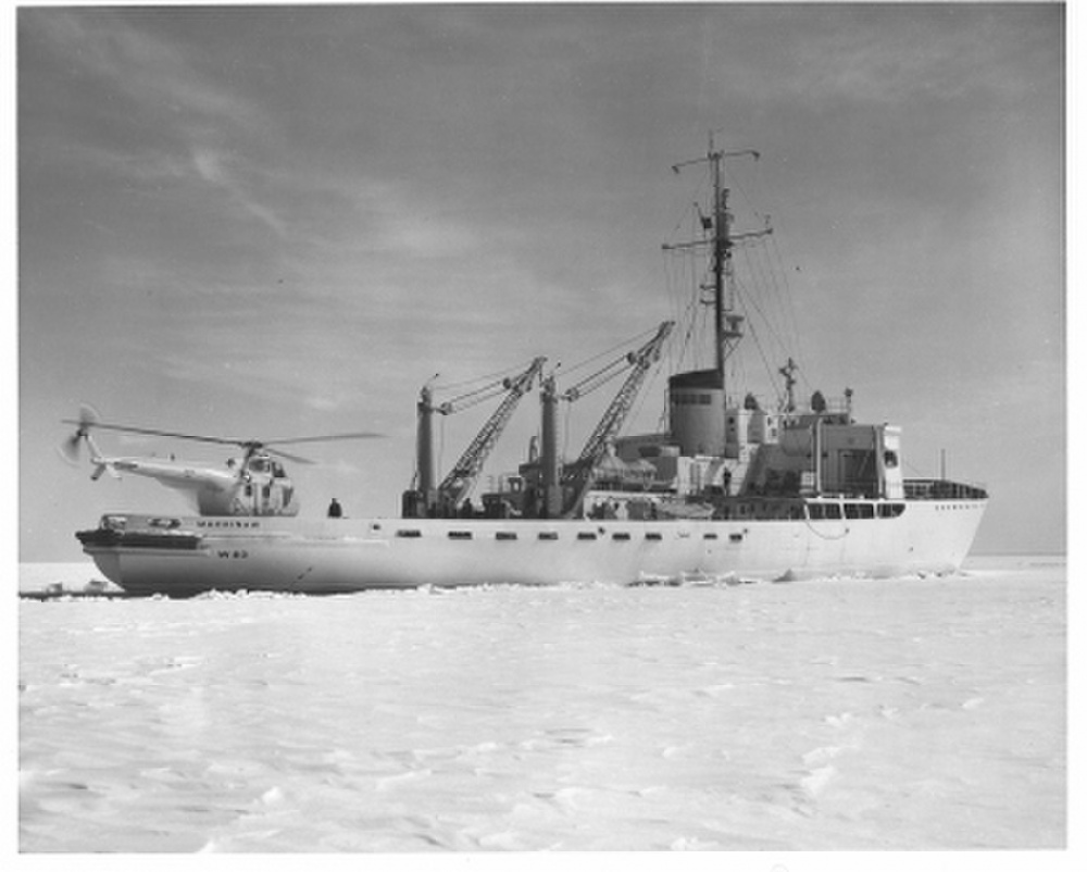 Black and white photo of Mackinaw from the 1950s showing a vintage helicopter on the fantail and the powerful derricks amidships. (U.S. Coast Guard Photo)